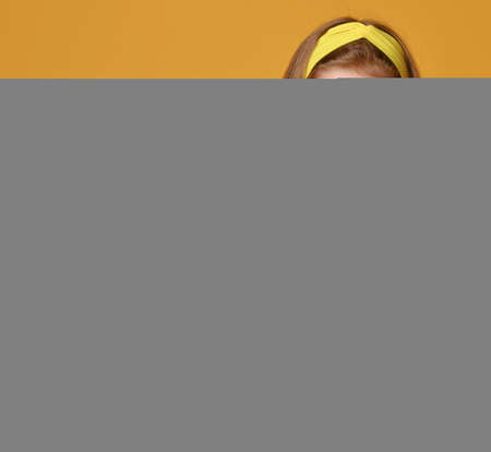 Happy cute red-haired kid girl in yellow t-shirt and colorful leggings sits on floor holding big...