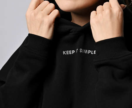 Closeup of chest and neck of woman in trendy black hoodie with inscription Keep it simple, holding...