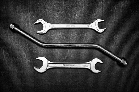Chrome wrenches and corrugated slim metal tube on the black table. top view, flat lay.