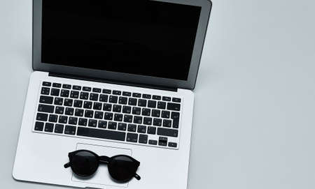 Stylish minimalistic workplace with laptop keyboard, black sunglasses in flat lay style. White background. Top view.の写真素材