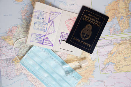 Passport with stamps next to a face mask and alcohol gel with map background. New ways of traveling.
