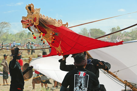 BALI, INDONESIA - JULY 15: Unidentified young men preparing to launch a huge kite decorated with a dragon head in adornments and crown, wings and long striped tail during the annual festival of traditional Balinese kites on the beach Galak in Bali island のeditorial素材