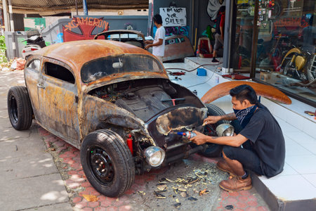 BALI, INDONESIA - MARCH 20: Young Balinese man cleans a body of an old volkswagen beetle during the making and vintage custom hotrod car in the auto and moto repair shop in Bali island on 20 March, 2015のeditorial素材
