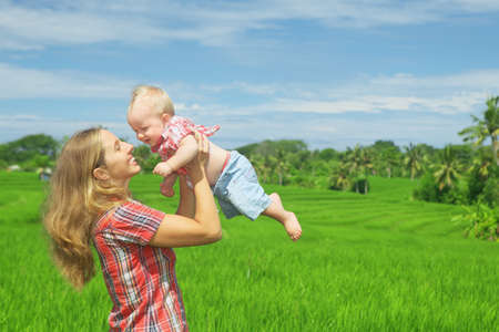 Happy mother tossing up joyful baby boy on Balinese green rice terraces background. Outdoors healthy child activity active lifestyle on family summer vacation with son on Indonesian tropical islandの写真素材