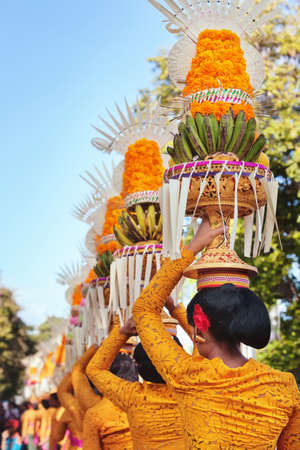 Procession of beautiful Balinese women in traditional costumes - sarong, carry offering on heads for...