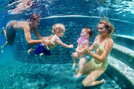 Happy family - 2 mothers with baby daughter and son and dive with fun in beach pool. Active parents...