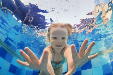 Funny face portrait of little baby girl swimming and diving underwater with fun in  pool. Active healthy lifestyle, water sport activity and lessons with parents on summer family vacation with child.の写真素材