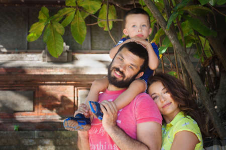 Face portrait of beautiful family - happy mother, father holding baby son on shoulders walk with fun. Active parents and people outdoor activity on tropical summer holiday with children on Bali islandの写真素材