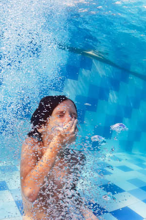 Funny portrait of boy swimming and diving in blue pool with fun - jumping deep down underwater with splashes and foam. Family lifestyle and summer children water sports activity with parents.の写真素材