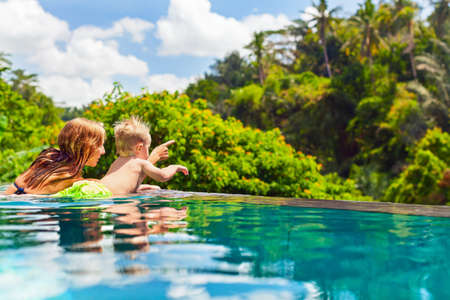 Family Bali beach holiday concept. Happy son with mother - active baby at poolside in infinity swimming pool. Summer healthy lifestyle and children water activity, games and lessons with parents.の写真素材