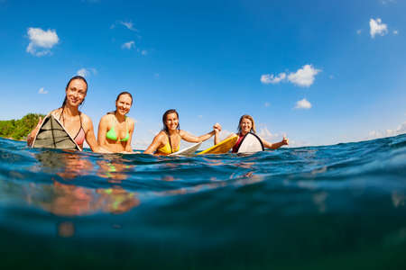 Happy girls in bikini have fun - group of surfers sit on surf boards, young women wait for big ocean wave. People in water sport adventure camp, beach extreme activity on summer beach family vacationの写真素材