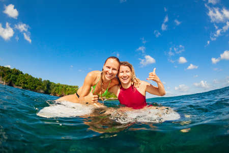 Happy girls in bikini have fun - group of surfers sit on surf boards, young women wait for big ocean wave. People in water sport adventure camp, beach extreme activity on summer beach family vacationの写真素材