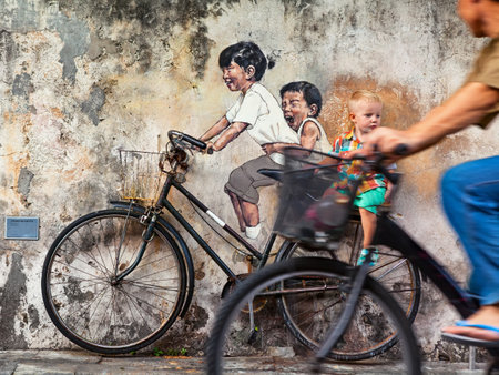 Georgetown, Penang, Malaysia - March 02, 2016: Cycling man look at little child siting on bicycle. Candid street scene. Background street art mural by artist Ernest Zacharevic.のeditorial素材