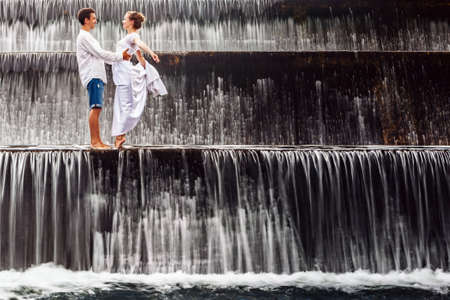 Happy family on honeymoon holidays - married loving couple hugging, kissing with fun under falling water in cascade waterfall pool. Active lifestyle, people travel on summer vacation on Bali island.の写真素材