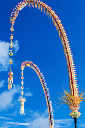 Traditional Bali Penjor, bamboo pole with decoration on village street in front of Balinese people house and temple on Galungan, Kuningan Hindu holidays. Indonesian art and culture. Travel backgroundの写真素材