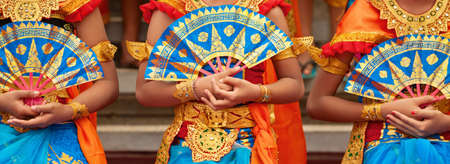 Asian travel background. Group of beautiful Balinese dancer women in traditional Sarong costumes with fans in hands dancing Legong dance. Arts, culture of Indonesian people, Bali island festivals.の写真素材
