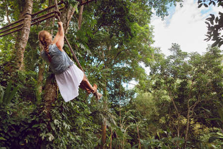 Family travel lifestyle. Happy young woman flying high with fun on rope swing on wild jungle background. Funny adventure walk in tropical rainforest. Leisure activity on summer vacation with kids.の写真素材