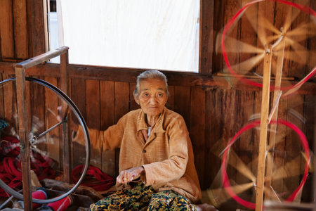 Inle Lake, Myanmar - January 04, 2007: Old woman of Intha people working at home in village on Inle lake in Shan state, spinning yarn by hand for traditional Burmese handmade textile.のeditorial素材