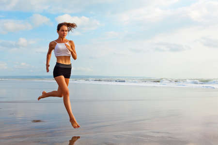 Barefoot sporty girl with slim body running along sea surf by water pool to keep fit and health....