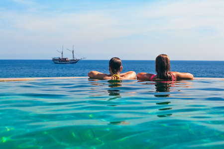 Happy young woman on summer beach holiday relaxing in luxury spa resort in infinity swimming pool with sea view. Healthy lifestyle, family travel background. Sailing yacht tropical island cruise.の写真素材