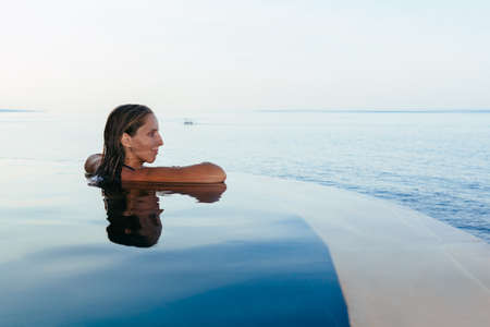 Black silhouette of happy woman on summer beach holiday relaxing in luxury spa hotel in infinity swimming pool with blue sea view. Healthy lifestyle, family travel background. Tropical island tour.の写真素材