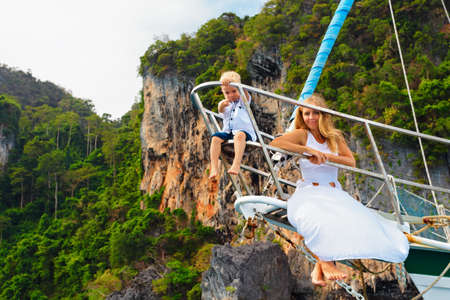 Happy family aboard. Young mother, little baby boy on board of sailing yacht. Child have fun discovering tropical islands in summer cruise. Travel adventure, yachting with kids on family vacation.の写真素材
