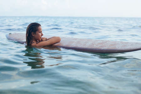 Joyful woman in have fun before surfing. Surfer girl hold surf board, look at sunset sky. People in...