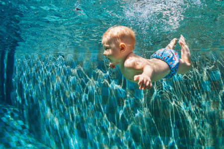 Happy child learn to swim, dive in blue pool with fun - jumping deep down underwater with splashes. Healthy family lifestyle, kids water sports activity, swimming lesson with parents in fitness clubの写真素材