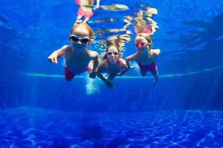 Happy family - mother, baby son, daughter in goggles swim, dive in pool with fun - jump deep down underwater. Healthy lifestyle, people water sport activity, swimming lessons on holidays with kidsの写真素材