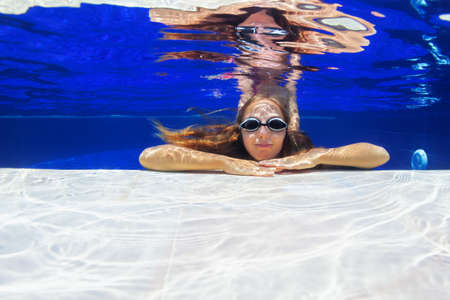 Happy family in swimming pool. Smiling young girl in goggles swim underwater, dive in pool with fun....
