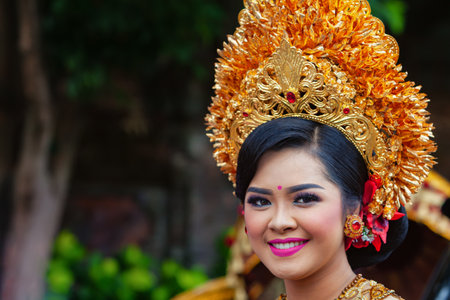 Denpasar, Bali island, Indonesia - June 23, 2018: Face portrait of beautiful young woman in traditional Balinese dance costume with golden headdress on street parade at art and culture festival.のeditorial素材