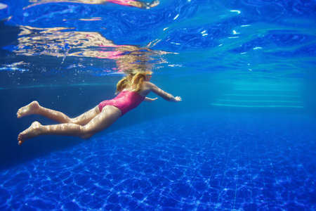 Happy family in swimming pool. Smiling child in goggles swim, dive in pool with fun - jump deep down underwater. Healthy lifestyle, people water sport activity, swimming lessons on holidays with kidsの写真素材