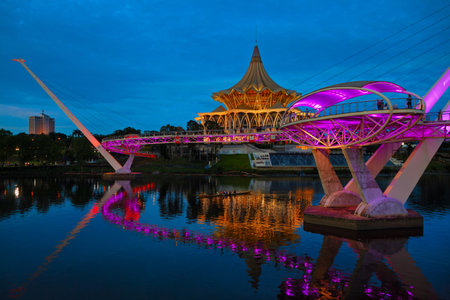 Kuching, Malaysia - March 11, 2019: Scenic night view of illuminated State Legislative Assembly and pedestrian bridge on Sarawak river. Waterfront landmark in Kota Kuching. Borneo travel destinations.のeditorial素材