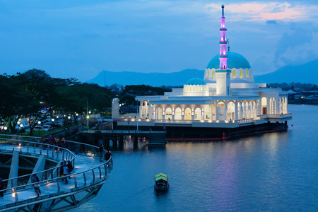 Kuching, Malaysia - March 15, 2019: Night view of illuminated floating mosque and people walking by pedestrian bridge on Sarawak river. Waterfront landmark in Kota Kuching. Borneo travel destinations.のeditorial素材