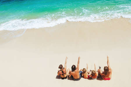 On sunny beach happy kids with parents have fun, sit on white sand see at sea surf with foam and...