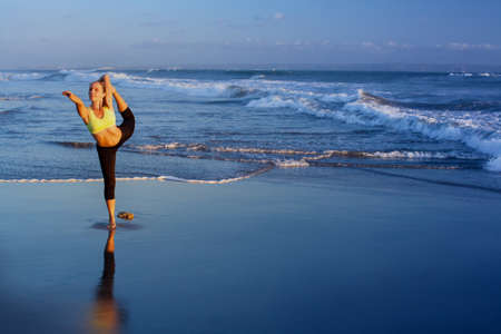 Young active woman stretching at yoga pose at spa retreat on sunset beach, ocean surf background. Travel lifestyle banner. Healthy people outdoor activity, family summer vacation on tropical island.の写真素材