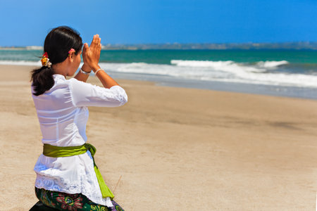 Bali island, Indonesia - March 18, 2015: Young balinese woman praying with namaste hands on sea beach at hindu ceremony before traditional religious holiday - silence day Nyepi.