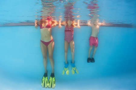 Happy family has fun, relax at poolside after swimming lesson. Underwater photo of people group in pool. Healthy lifestyle, active parents, people water sports activities on summer holidays with kids.の写真素材