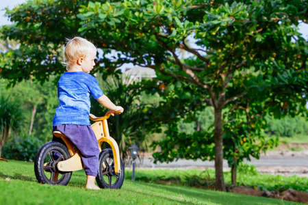 2 - 3 years joyful boy riding a wooden balance bike (run bike). Happy barefoot child learning to wheel, keep balance on training bicycle in the garden. Active kid playing outside. First day on bike.の写真素材