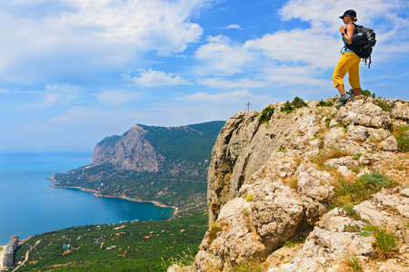 Young active woman stand on mount top. Look at amazing sea landscape. Family travel adventure, hiking activity, healthy lifestyle, exploring nature on summer vacation. Weekend day walking tour.の写真素材