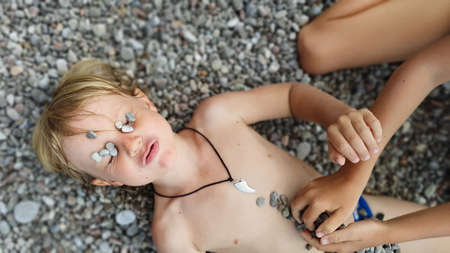 On sunny beach happy kids have fun, lying down on hot pebble, sunbathing, warming after swimming in...