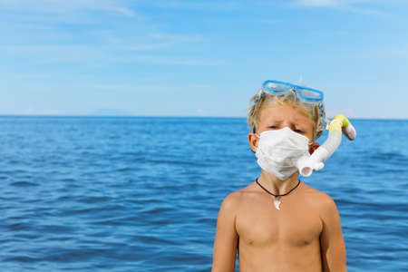 Boy in snorkeling mask wear surgical face mask on sea beach. Cancelled cruises, tours due coronavirus COVID 19 world epidemic. Travel ban for family vacation, tourism industry crisis at summer 2020の写真素材