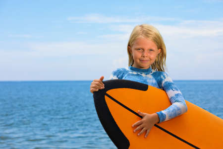 Happy baby girl - young surfer learn to ride on surfboard with fun on sea waves. Active family lifestyle, kids outdoor water sport lessons, swimming activity in surf camp. Summer vacation with child.の写真素材