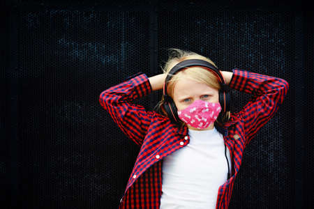 Young positive child in headphones listening music with fun raise hands up. Funny girl wear stylish...