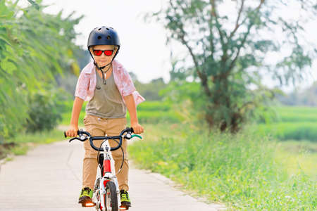 Country cycling walk. Young rider kid in helmet and sunglasses riding bicycle. Happy child have fun on empty trail. Active family lifestyle, sports, outdoor recreational activities on summer holidays.の写真素材