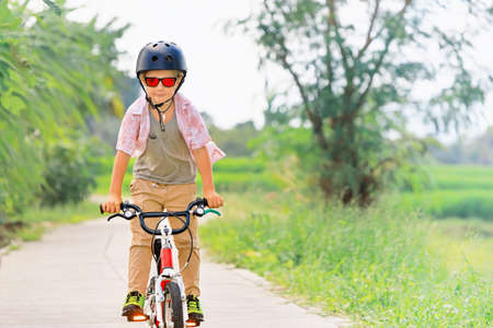 Country cycling walk. Young rider kid in helmet and sunglasses riding bicycle. Happy child have fun on empty trail. Active family lifestyle, sports, outdoor recreational activities on summer holidays.の素材 [FY310156967603]