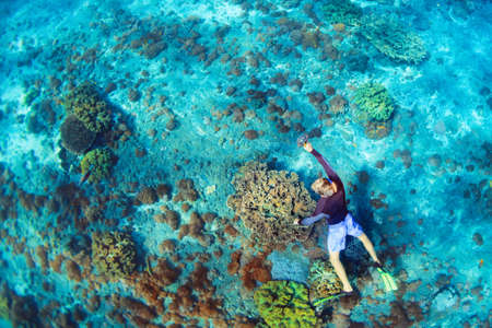 Happy family vacation. Man in snorkeling mask with camera dive underwater with tropical fishes in...