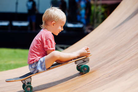 Funny skateboard riding. Little child with surf skateboard have fun in beach skate park. Active...
