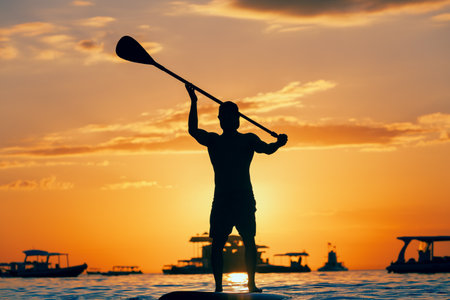 Active paddle boarder. Black sunset silhouette of young sportsman paddling on stand up paddleboard. Healthy lifestyle. Water sport, SUP surfing tour in adventure camp on family summer beach vacation.の写真素材