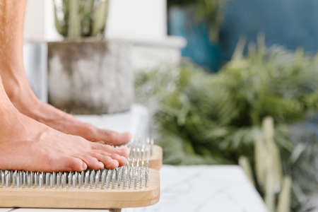Outdoor practice of standing on nails at summer yoga retreat. Young barefoot person stand on sadhu board with sharp metal nails. Closeup view of sadhu wooden board for yoga practice.の写真素材